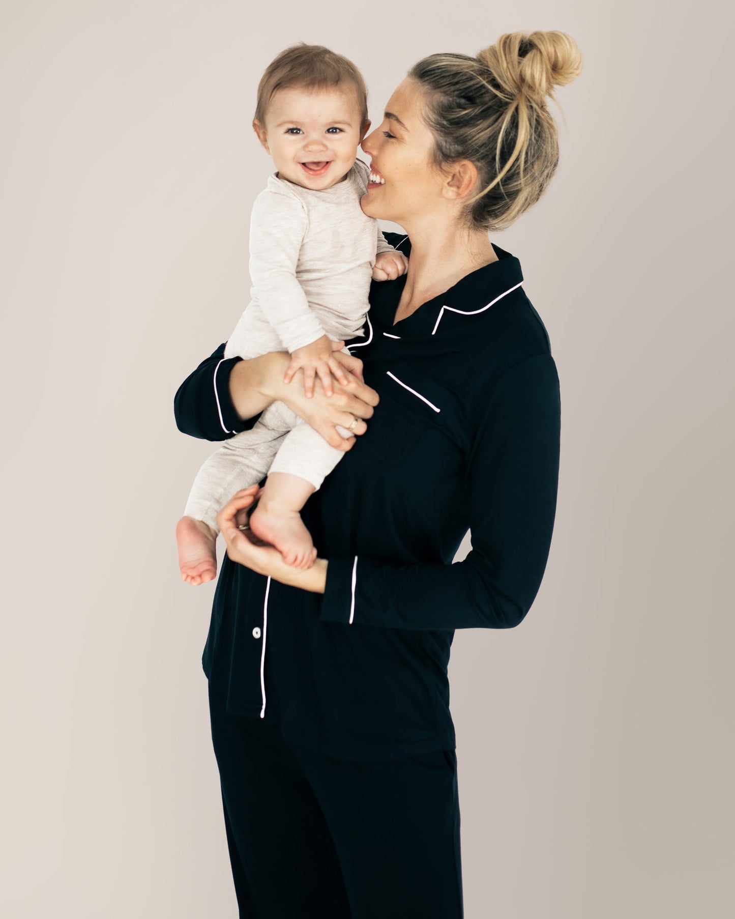 Model wearing the Clea Bamboo Long Sleeve Pajama Set in Black holding her baby on her hip. @model_info:Karin is 5'9" and wearing a Medium.