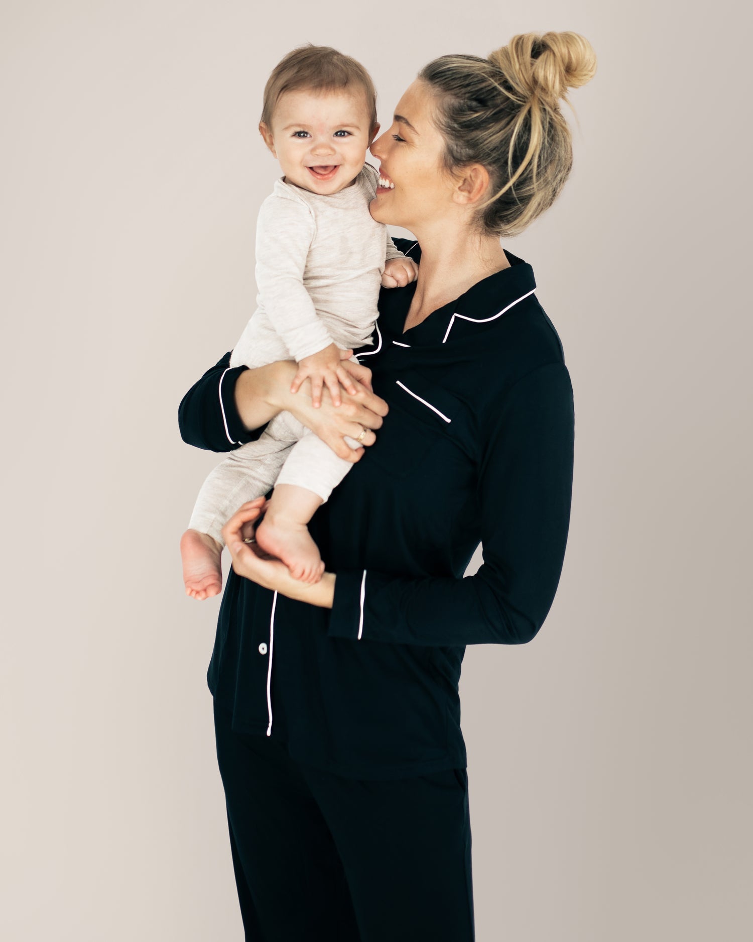 Model wearing the Clea Bamboo Long Sleeve Pajama Set in Black holding her baby on her hip. @model_info:Karin is 5'9" and wearing a Medium.